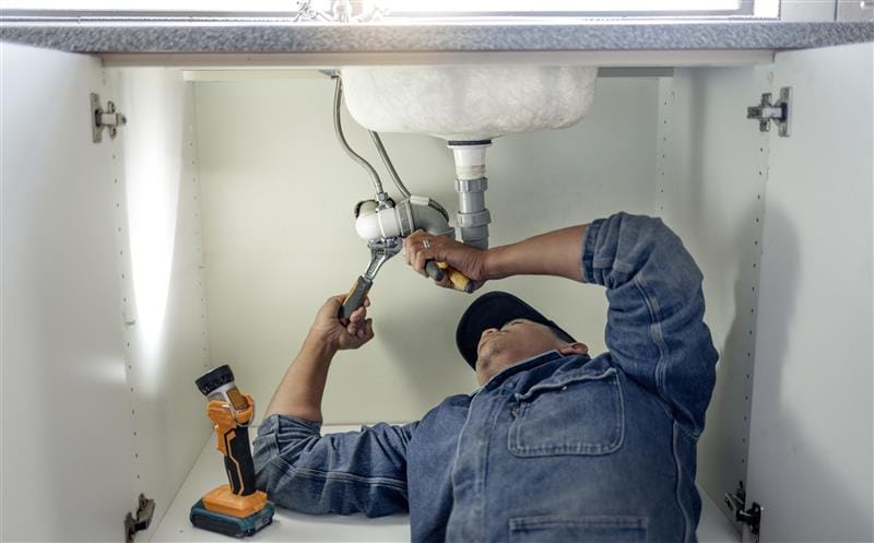 Plumber repairing pipes beneath a bathroom sink in Seaside
