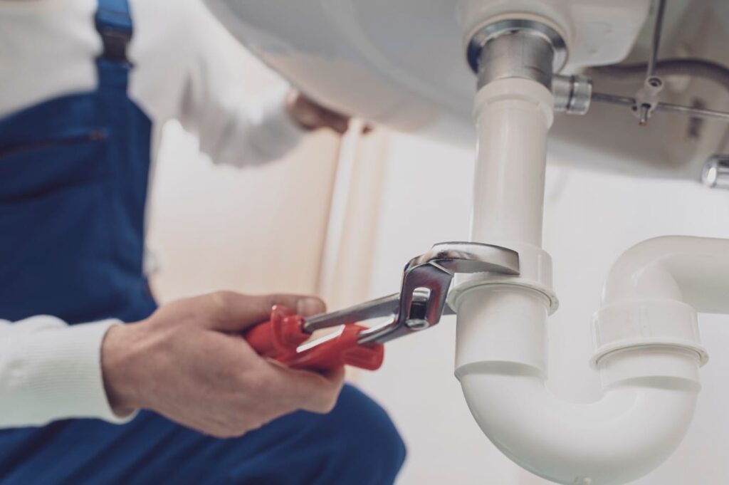 Plumber repairing a white drain pipe beneath a sink in Seaside