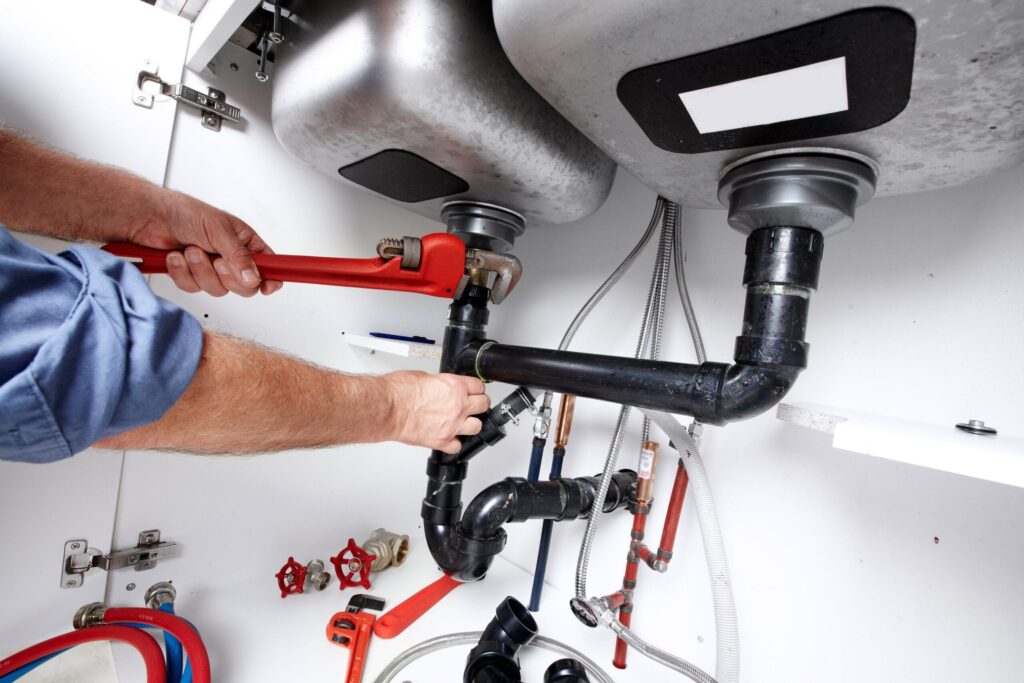 Plumber repairing drain pipes beneath a kitchen sink in Seaside